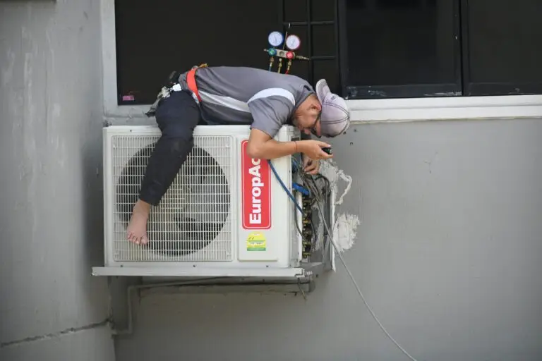 A technician skillfully repairing an outdoor air conditioning unit mounted on a building wall.